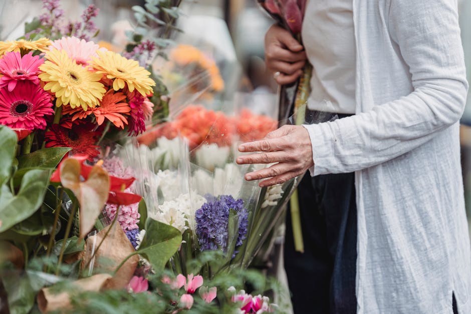 A person dressed in a light-colored, long-sleeved jacket is selecting a floral bouquet at a flower shop, Flowers Radlett, near Radlett station WD7. The bouquet features a vibrant arrangement of fresh 