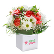This joyful bouquet seems to gather the very essence of a Radlett spring morning, arranged in a chic white gift bag ready for delivery or surprise. A vibrant cascade of coral and peach carnations delivers both softness and exuberance, their layered petals offering a rich, tactile presence. Sprightly white daisies, each glowing with a golden-green heart, stand alongside, infusing the arrangement with friendliness and charm reminiscent of open local meadows. Wisps of white baby's breath flicker throughout, adding hints of innocence and a sense of drifting lightness. Subtle purple-tipped buds tucked along the edge provide not just colour, but the suggestion of growth and renewal-much like walking past budding hedgerows in early April. Deep, glossy leaves cradle the entire bouquet, forming a lush, protective embrace reminiscent of Radlett's tree-lined avenues. Every flower is thoughtfully placed by expert florists, giving the bouquet a full, rounded shape that conveys both freshness and abundance. The clean white bag with elegant ribbon handles signals a gift designed to create joy-perfect for birthdays, congratulatory messages, or simply brightening a loved one's day along the High Street. This arrangement radiates sincerity and warmth, making it an irresistible choice for those seeking to send a meaningful gesture throughout Radlett.