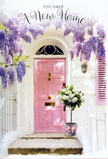 The image presents a serene, storybook-like doorway that feels perfectly at home in Radlett, perhaps on a quiet side street not far from the village centre. A pale pink front door, painted in soft, chalky tones, serves as the focal point, flanked by whitewashed walls and a single matching shutter that hints at a well-kept, much-loved house. Flowing down from above, wisteria blooms in generous clusters of lavender and lilac, their trailing shapes forming a loose curtain over the entrance. The blossoms look full and feathery, with individual petals catching the light and casting tiny, dappled patterns on the door and step, evoking the gentle fragrance that often drifts through Radlett gardens in late spring. At ground level, centred on the doorstep, sits a simple, stylish grey bucket, the kind a local florist might choose for its understated charm. It overflows with white and cream roses, each flower open and rounded, petals layered in lush, velvety rings that almost spill over the rim. Pockets of soft green foliage peek between the roses, adding an airy, garden-fresh feeling, as though the blooms had just been brought in from a nearby border. Tied around the bucket is a delicate pink ribbon, its colour echoing the door and giving the arrangement a subtle, celebratory touch. Natural light washes in from one side, lending the scene a calm, late-afternoon glow and softening every edge. The overall impression is of a heartfelt housewarming gesture: a fragrant, welcoming arrangement left on the step of a new Radlett home, offering comfort, good wishes, and the promise of many warm days to come.